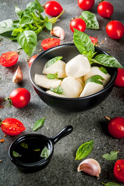 Prodotti biologici crudi dell'azienda agricola. cottura della cena in stile italiano. ingredienti per insalata caprese, pasta, pizza. basilico, pomodori, mozzarella, olio d'oliva. tavolo in pietra grigio scuro. copia spazio