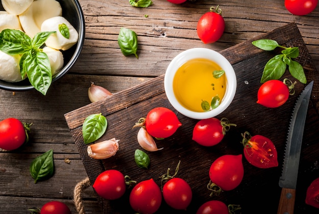 Farm raw organic products. Preparation of dinner in the Italian style. Ingredients for caprese salad, pasta, pizza. Basil, tomatoes, mozzarella cheese, olive oil on an old wooden table.