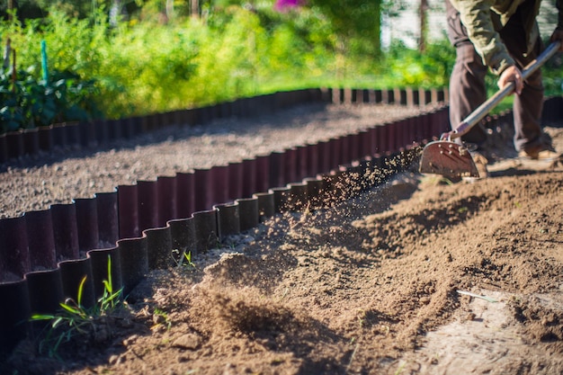 Farmer cultivating land in the garden with hand tools soil\
loosening gardening concept agricultural work on the\
plantation