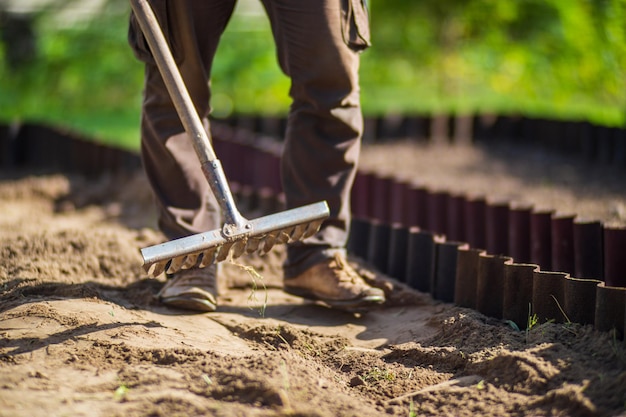 Contadino che coltiva la terra in giardino con attrezzi manuali allentamento del suolo concetto di giardinaggio lavori agricoli nella piantagione