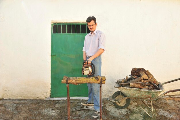 Farmer cutting firewood in a rural village, with chainsaw and wheelbarrow