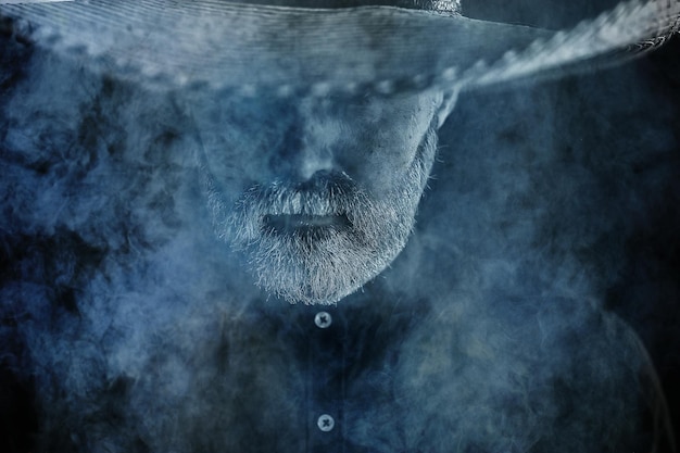 фермер-хипстер в соломенной шляпе с полями в дыму курит табак в стиле ретро дикий запад самбреро