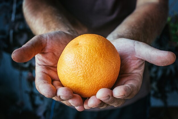 A farmer holding an orange with dirty hands.