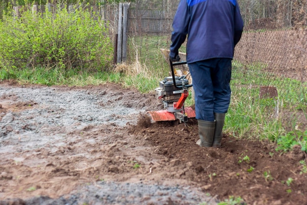 農民、男性は耕運機で土地を耕し、ジャガイモや他の作物を植えるために土地を準備します。