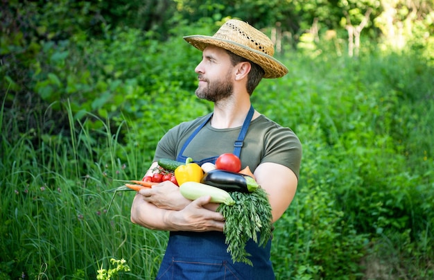 麦わら帽子をかぶった農家の男性は、新鮮な熟した野菜を保持します