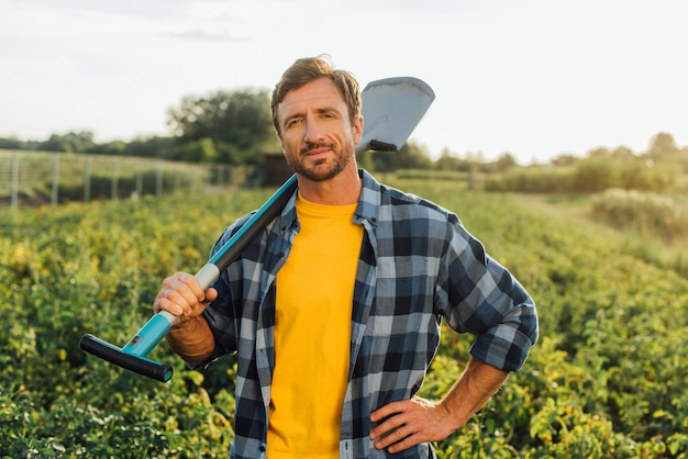 Farmer in plaid shirt looking at camera while holding shovel in field