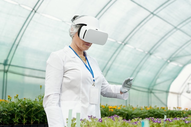 Farmer or researcher in vr headset standing in front of flower seedlings