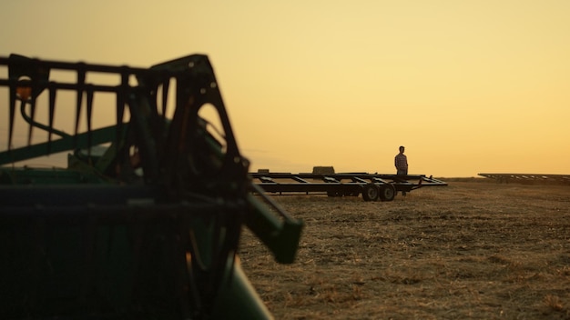 Farmer silhouette at wheat field harvesting equipment at golden sunset time