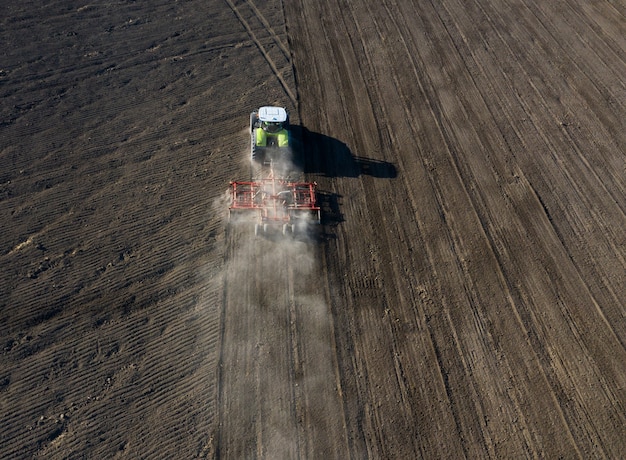 Un agricoltore su un trattore prepara la terra con un coltivatore di semina come parte del lavoro di pre-semina all'inizio della stagione agricola primaverile su terreno agricolo.