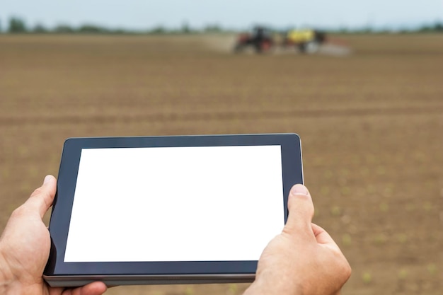 Farmer using tablet computer in agricultural cultivated field. White screen.