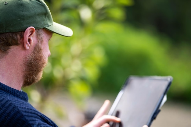 Farmer wearing a hat being sun smart using technology and a tablet and phone in a field studying a soil and plant sample in field