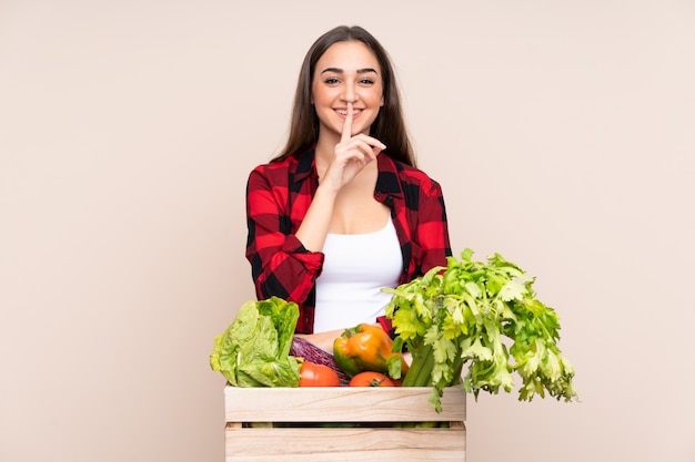 Farmer with freshly picked vegetables in a box on beige doing silence gesture