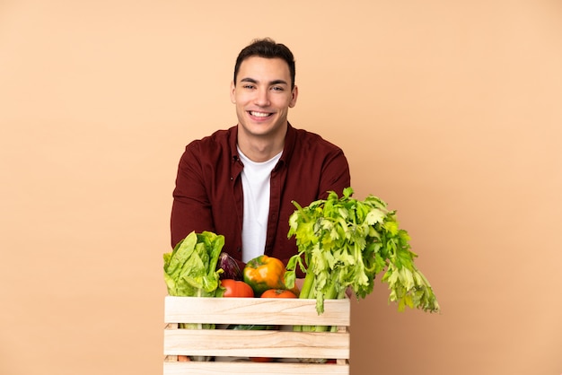 Farmer with freshly picked vegetables in a box on beige wall keeping the arms crossed
