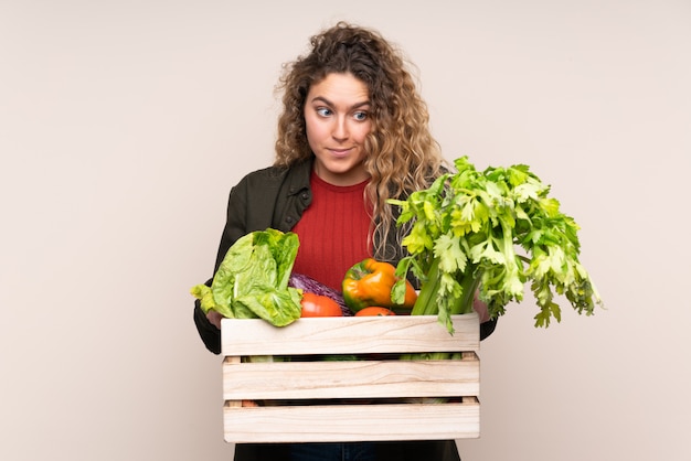 Farmer with freshly picked vegetables in a box on beige wall