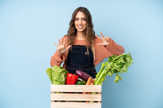 Farmer with freshly picked vegetables in a box counting eight\
with fingers