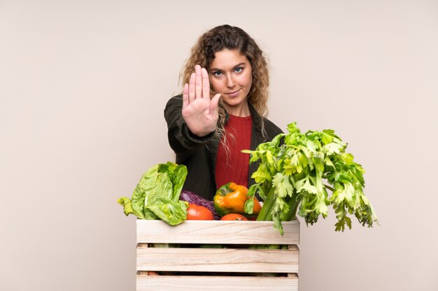 Farmer with freshly picked vegetables in a box isolated on beige making stop gesture with her hand