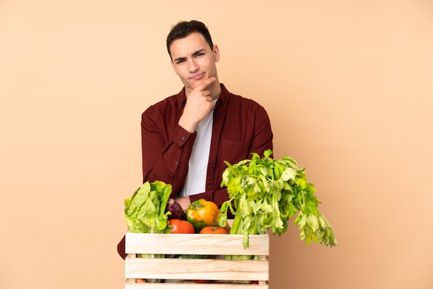 Farmer with freshly picked vegetables in a box isolated on beige wall thinking