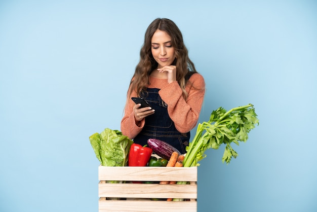 Farmer with freshly picked vegetables in a box thinking and sending a message