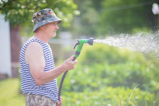 写真 夏に野菜植物に水をまく庭のホースと銃のノズルを持つ農家ガーデニングのコンセプトベッド列で成長している農業植物