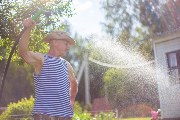 写真 ガーデンホースと銃のノズルを使った農夫が夏に野菜の植物に水を注ぐ ガーデニングコンセプト 床の列で育つ農業植物