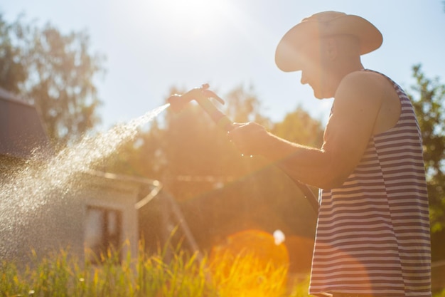 写真 ガーデンホースと銃のノズルを使った農夫が夏に野菜の植物に水を注ぐ ガーデニングコンセプト 床の列で育つ農業植物