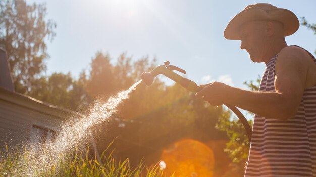 사진 정원 호스 및 총 노즐을 가진 농부는 여름에 채소 식물에 물을 주고 정원 개념 농업 식물은 침대 줄에서 자란다
