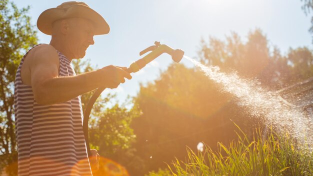 写真 ガーデンホースと銃のノズルを使った農夫が夏に野菜の植物に水を注ぐ ガーデニングコンセプト 床の列で育つ農業植物