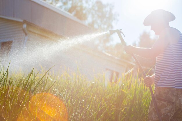 写真 ガーデンホースと銃のノズルを使った農夫が夏に野菜の植物に水を注ぐ ガーデニングコンセプト 床の列で育つ農業植物