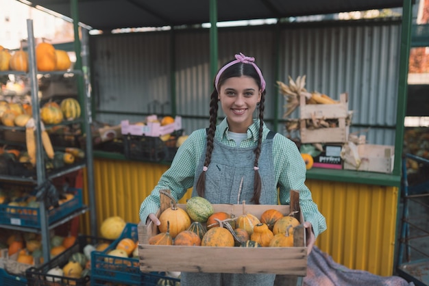 Farmer woman holds a wooden box with pumpkins in hands