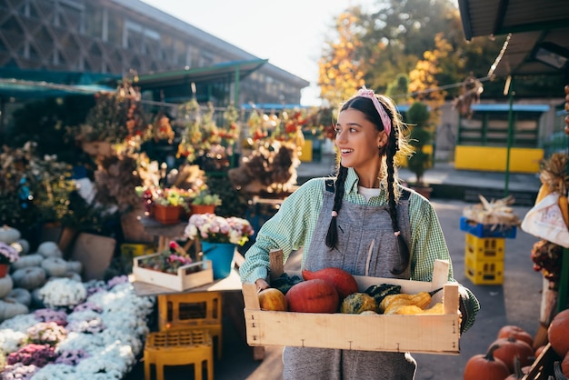 Photo farmer woman holds a wooden box with pumpkins in hands