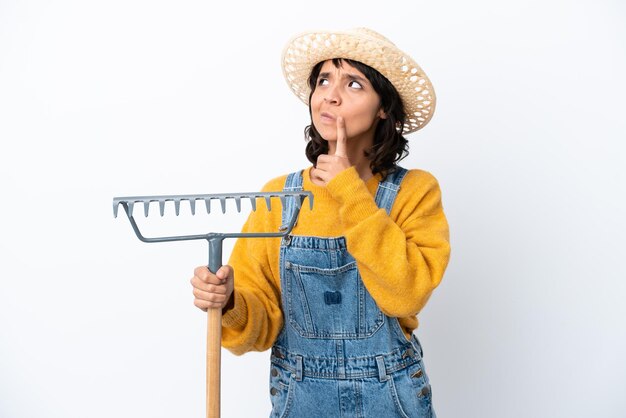 Farmer woman isolated on white background having doubts while looking up