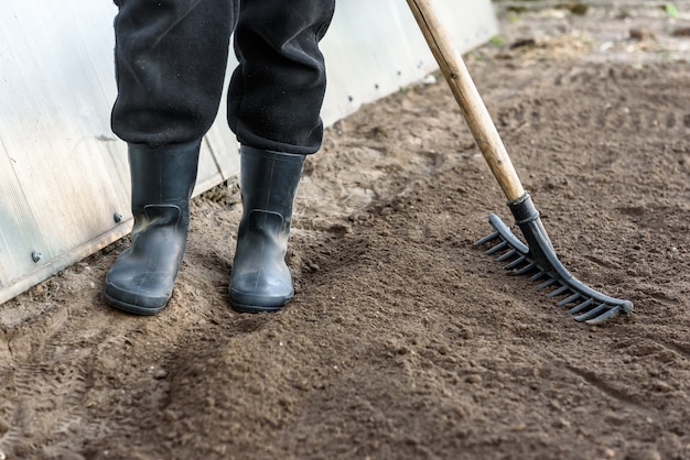 Farmer working in garden with rake leveling ground. Preparation of ground for planting.