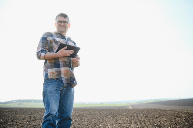 Farmer works in field in spring with tablet An elderly farmer looks at tablet and green shoots A smart agronomist with tablet in his hands checks field Environmentally friendly farming