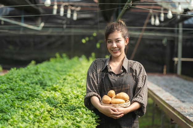 新鮮な有機野菜でいっぱいの木製バスケットを保持している農家の若い女性