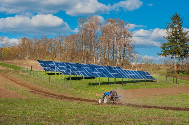 Foto trattore di agricoltori aratura, lavoro primaverile sul campo e pannello solare con cielo nuvoloso