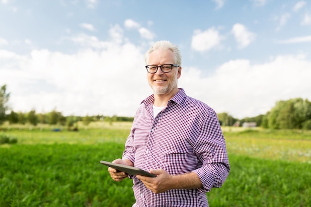 farming, agriculture, technology, old age and people concept - happy senior man with tablet pc computer at county or farm