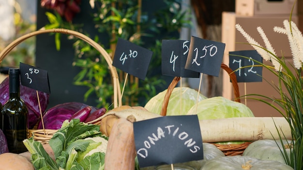 写真 地元産の野菜やワインのボトル、ビジネス寄付のためのコインが入った瓶でいっぱいの農場屋台。有機レタスまたはキャベツ、生のカボチャ、ズッキーニを含むグリーンマーケット。閉じる。