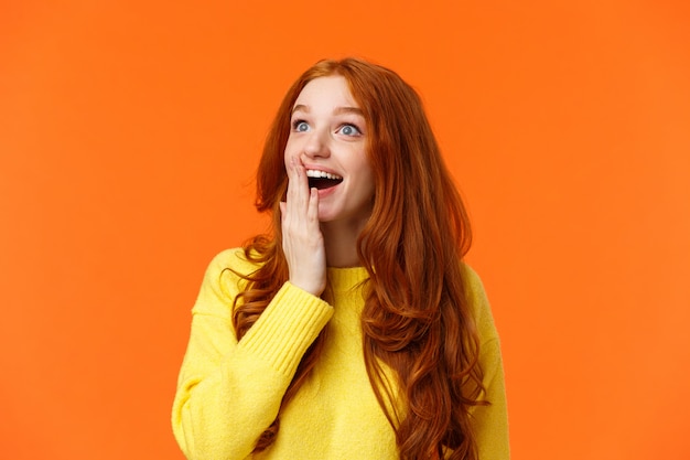 Fascinated and amiring cute redhead woman looking impressed and excited at upper left corner