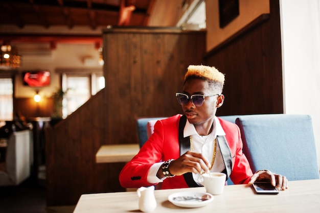 Fashion african american man model at red suit with highlights hair and sunglasses sitting at cafe with coffee