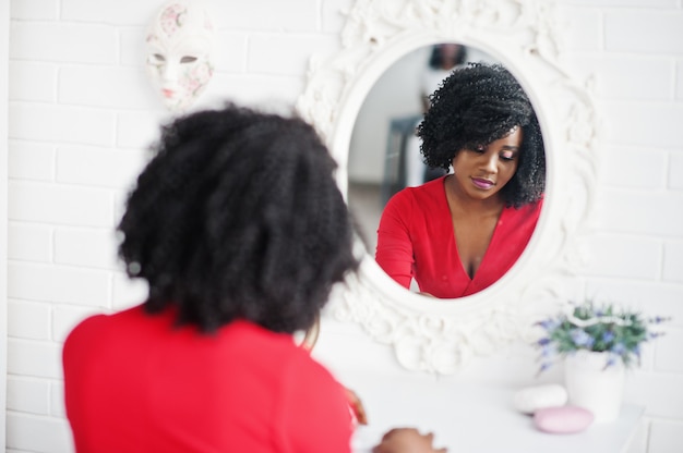 Fashion african american model in red beauty dress, sexy woman posing evening gown and looking at mirror.