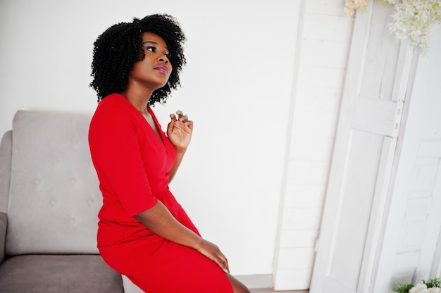 Fashion african american model in red beauty dress, sexy woman posing evening gown in white vintage room.