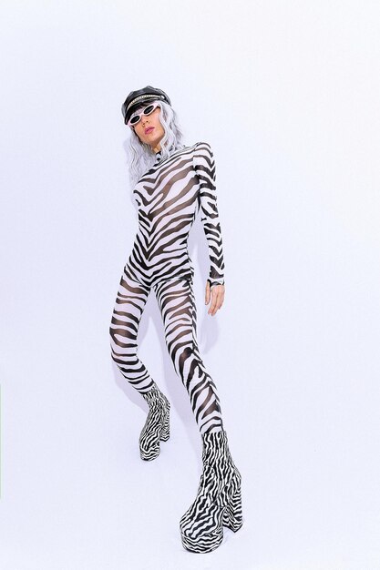 Fashion androgenic blonde model in freak stylish zebra print clothes and boots posing in a white studio. Accessory trend leather cap