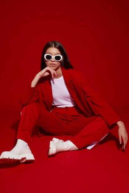 Модная азиатская модель в красном костюме, белых сапогах и солнцезащитных очках.