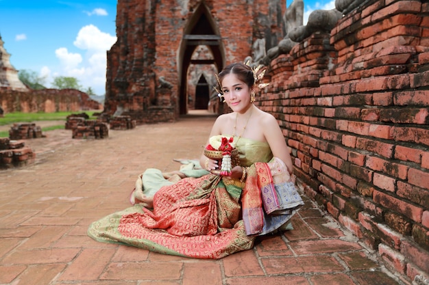 Fashion asian girl in Thai traditional costume in ancient temple with steering wheel flower in hand