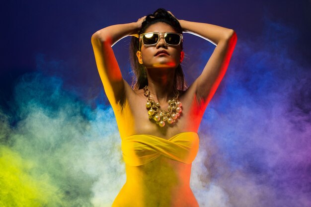 Fashion Asian Woman Tan skin black hair beautiful high fashion make up sunglasses pearl necklace accessories wear yellow bikini. Studio Lighting Dark smoke Background copy space text logo