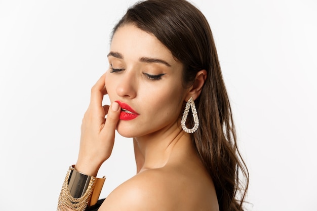 Fashion and beauty concept. Tender and feminine brunette woman touching red lips and looking down sensually, standing over white background