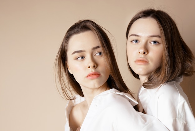 Fashion beauty models two sisters twins beautiful nude girls looking at the camera isolated on beige background