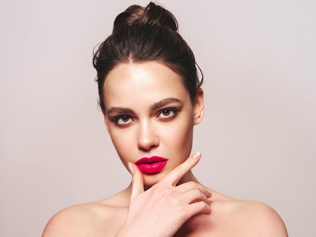 Fashion beauty portrait of young brunette woman with evening stylish makeup and perfect clean skin Sexy model with hair in a bun posing in studio With pink bright natural lips