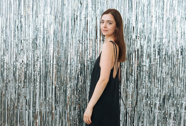 Fashion beauty portrait of young woman with dark long hair on evening elegant black dress with open back on the sparkle background