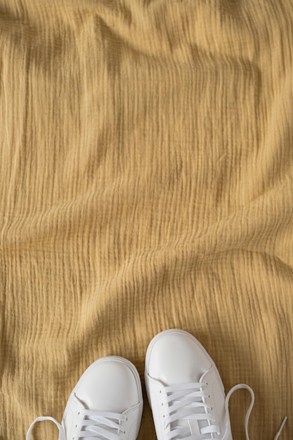 Модный блог или концепция журнала Белые женские кроссовки на фоне желтой мятой муслиновой ткани Плоский вид сверху минимальный фон